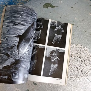 May include: Black and white photograph of a book open to a page with a leaping fish and a series of four images of a child. A white lace doily is in the corner.