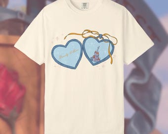 Op de afbeelding: Crèmekleurig T-shirt met een hartvormig ontwerp. Het ontwerp toont twee lichtblauwe harten, één met de tekst "Beauty Within" en de andere met een kasteelillustratie, verbonden door een gouden lint.