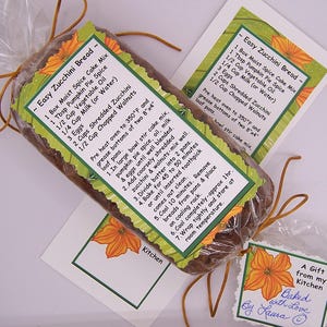 May include: A wrapped loaf of zucchini bread, tied with brown twine. The packaging includes recipe cards with green borders and orange floral designs. A small gift tag is also attached, with the text "Baked with Love".