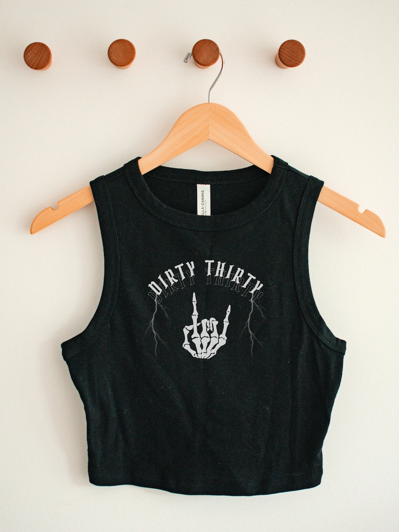 May include: Black sleeveless crop top with a white graphic print of a skeleton hand giving the middle finger with lightning bolts and the text "Dirty Thirty".