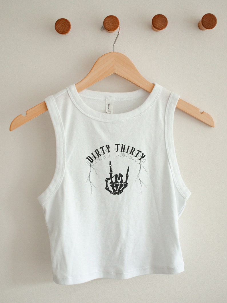 May include: White sleeveless crop top with a black graphic print of a skeleton hand making a rock and roll sign with the text "Dirty Thirty" above it.