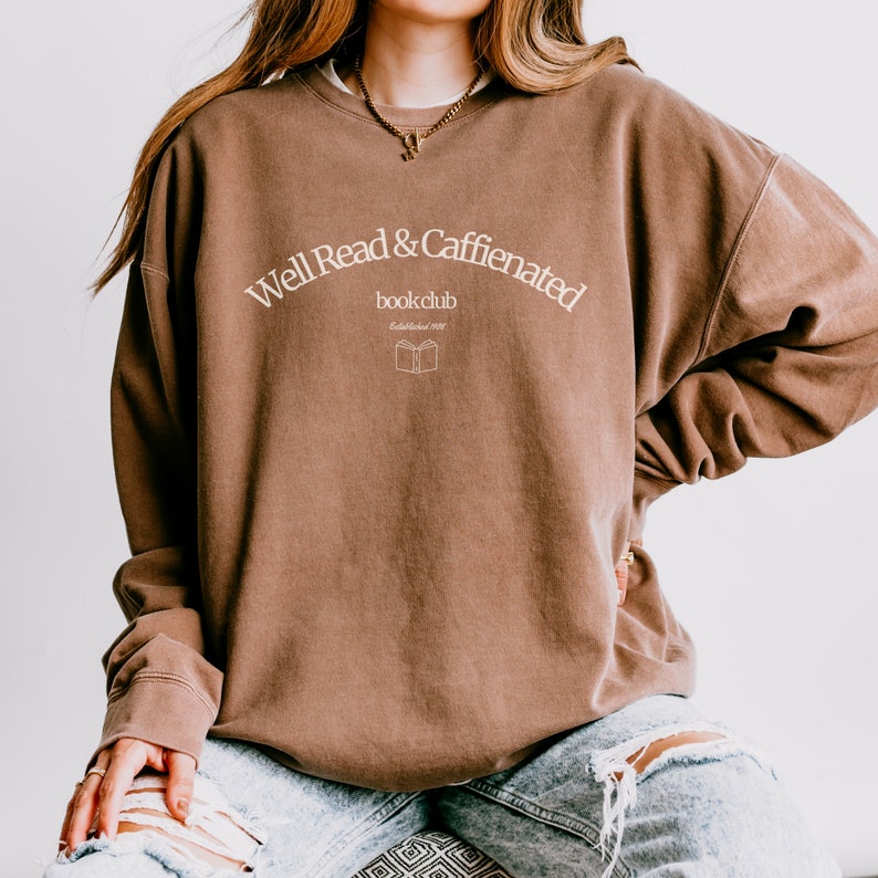 Puede incluir: Una sudadera marr&oacute;n con el texto "Well Read & Caffeinated book club Established 2022" en blanco.