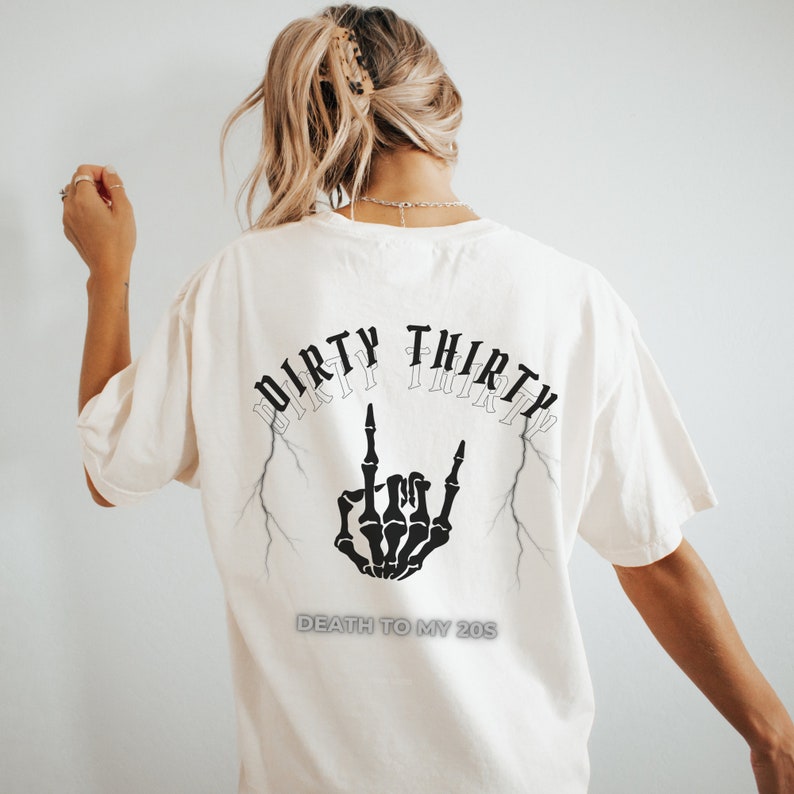 May include: Cream-colored t-shirt with a black graphic on the back. The graphic features the words "DIRTY THIRTY" above a skeleton hand making a rock and roll gesture, with the text "DEATH TO MY 20S" below.