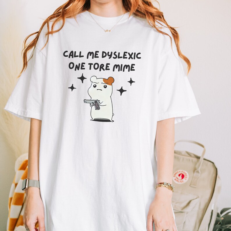 May include: White t-shirt with a cartoon hamster holding a gun and the text "Call me dyslexic one tore mime" printed on it.
