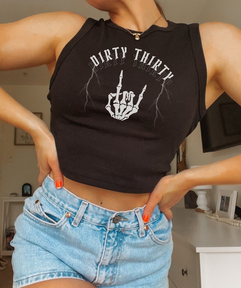 May include: Black sleeveless crop top with the text "Dirty Thirty" and a skeleton hand making a rock and roll hand gesture. The top has lightning bolts on either side of the text.