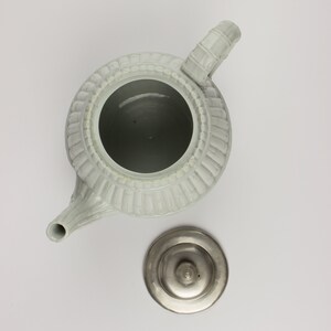 May include: A white ceramic teapot with a fluted design and a silver lid. The teapot has a spout and a handle.