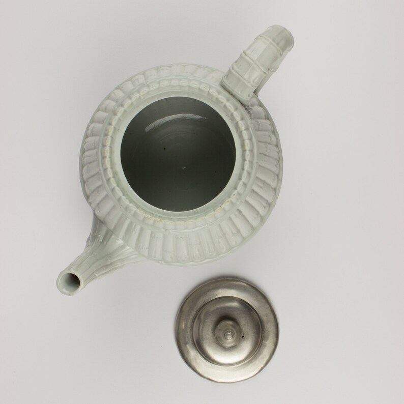 May include: A white ceramic teapot with a fluted design and a silver lid. The teapot has a spout and a handle.