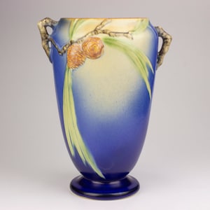 Puede incluir: Un jarrón de cerámica azul con dos asas y un diseño de piña. El jarrón tiene un esmalte amarillo claro y azul.