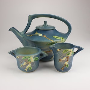 May include: A blue ceramic teapot and two creamer pitchers with a floral design. The teapot has a unique shape with a curved spout and handle. The creamer pitchers are smaller and have a more traditional shape.