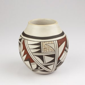 May include: A white ceramic pot with a geometric design in black, brown, and white. The pot has a rounded shape and a wide mouth.