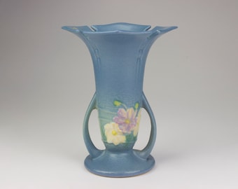 Könnte beinhalten: Eine blaue Keramikvase mit zwei Henkeln und einem Blumendesign. Die Vase hat eine breite Öffnung und einen schmalen Boden.
