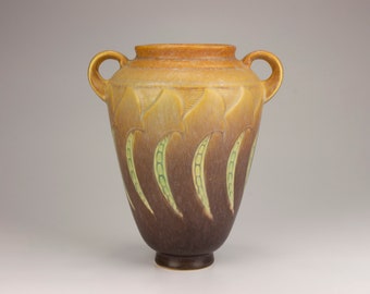 May include: A brown and yellow ceramic vase with two handles and a green and brown design of pea pods.