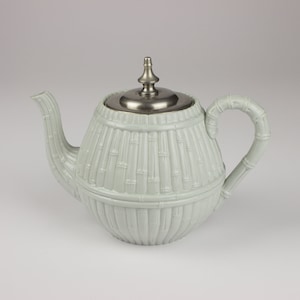 May include: A light green ceramic teapot with a silver lid and a bamboo-like design. The teapot has a round body and a curved spout.