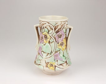 May include: A white ceramic vase with two handles and a floral design. The vase features a raised design of purple, yellow, and green morning glory flowers.