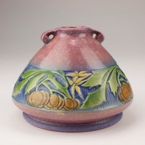 May include: A pink ceramic vase with a wide base and two handles. The vase is decorated with a floral design in shades of green, blue, and yellow.