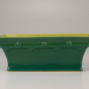 May include: A rectangular green ceramic planter with a yellow rim and a decorative design around the top edge.