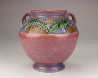 May include: A large, round ceramic vase with two handles. The vase is primarily a speckled mauve colour, with a band of blue and a decorative relief of green leaves, yellow flowers, and brown fruit. The base and rim are a darker purple.