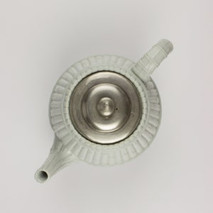 May include: A light blue ceramic teapot with a silver lid and a decorative design around the top. The teapot has a spout and a handle.