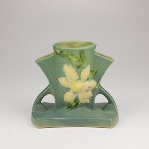 May include: A green ceramic vase with a yellow flower design. The vase has two handles and a wide base.