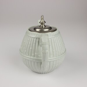 May include: A white ceramic teapot with a silver lid and a bamboo design. The teapot is round and has a handle on the side.