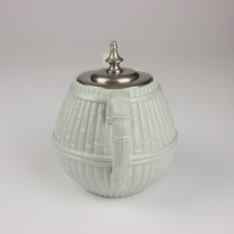 May include: A white ceramic teapot with a silver lid and a bamboo design. The teapot is round and has a handle on the side.