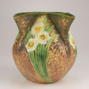 May include: A brown and green ceramic vase with a textured surface and a floral design of white daffodils.