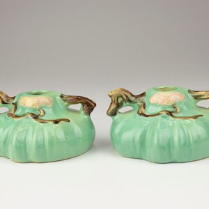 May include: A pair of green ceramic candle holders with brown handles shaped like branches. The holders have a textured surface and a small opening in the center for a candle.