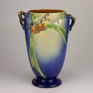 May include: A blue and cream glazed ceramic vase with two handles and a pine cone design.