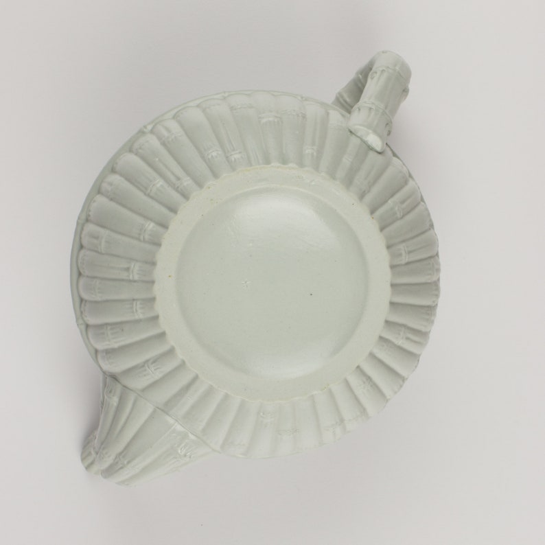 May include: A white ceramic teapot with a bamboo-like design. The teapot has a round body and a spout on the side. The handle is shaped like a bamboo stalk.