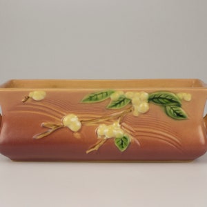 May include: A rectangular planter with two handles, made of glazed ceramic. The planter is decorated with a floral design in shades of pink, yellow, and green.