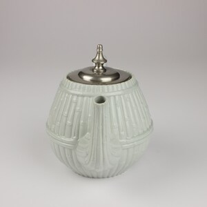 May include: A white ceramic teapot with a silver lid and a bamboo-like design. The teapot has a rounded body and a spout on the side.