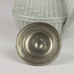May include: A silver teapot lid with a bamboo design. The underside of the lid has a circular metal base with the text "Art Metal Germany" inscribed on it.