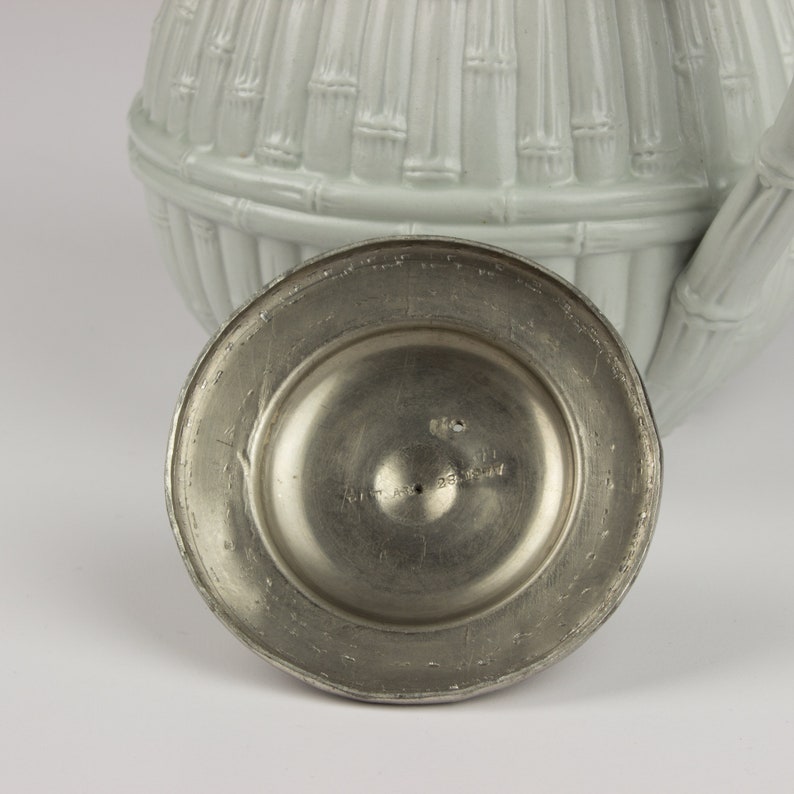 May include: A silver teapot lid with a bamboo design. The underside of the lid has a circular metal base with the text "Art Metal Germany" inscribed on it.