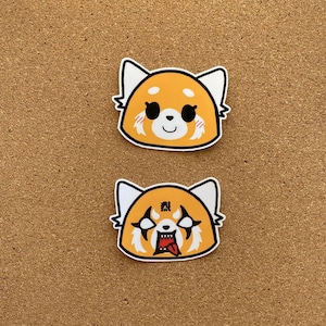 May include: Two red panda stickers, one with a cute expression and the other with a fierce expression. The stickers are on a brown corkboard background.