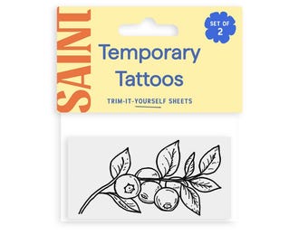 May include: A package of temporary tattoos featuring a black and white illustration of blueberries on a branch with leaves. The package is labeled "Temporary Tattoos" and "Trim-It-Yourself Sheets". The brand name "SAINT" is visible.