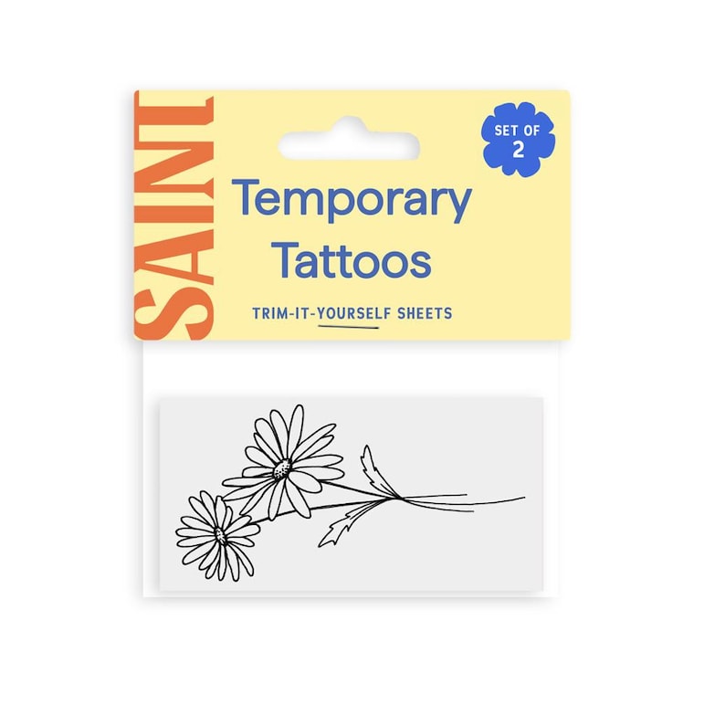 Pu&ograve; includere: Un pacchetto di tatuaggi temporanei con un disegno di margherite in bianco e nero. La confezione include una scheda gialla e bianca con le parole "Temporary Tattoos" e "Trim-It-Yourself Sheets". La scheda ha anche la parola "SAINT" in arancione.