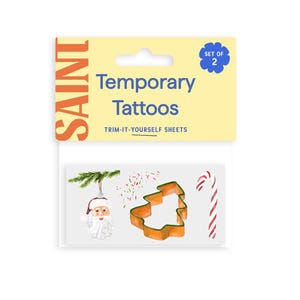May include: A sheet of temporary tattoos featuring Christmas-themed designs. The designs include a Santa Claus ornament, a Christmas tree, and a candy cane. The packaging is yellow with the word "SAINT" in orange.