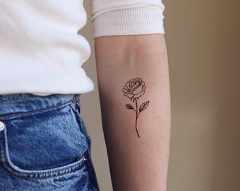 Puede incluir: Un simple dibujo de línea de un tatuaje de rosa en el brazo de una persona.