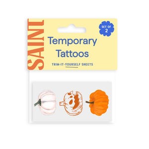 May include: A set of two temporary tattoo sheets featuring pumpkin designs. The designs include a white pumpkin, a jack-o'-lantern, and an orange pumpkin. The packaging has the word "SAINT" and the words "Temporary Tattoos" printed on it.