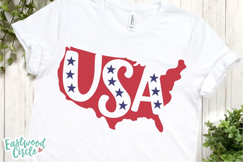 May include: White t-shirt with a red outline of the United States with the word "USA" in white letters and blue stars inside the letters and outline.