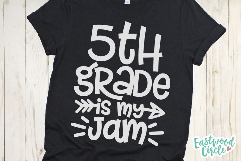 Op de afbeelding: Zwart T-shirt met witte tekst die "5th grade is my jam" luidt met pijlen en lijnen aan beide kanten van de tekst.