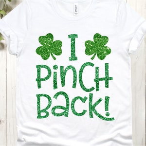 Puede incluir: Camiseta blanca con tr&eacute;boles de purpurina verde y el texto "I Pinch Back!"