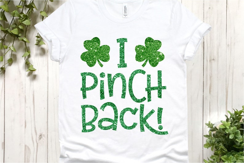 Puede incluir: Camiseta blanca con tr&eacute;boles de purpurina verde y el texto "I Pinch Back!"