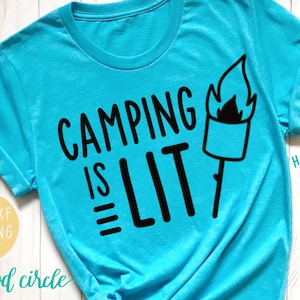 以下が含まれることがあります： ターコイズブルーのTシャツに、黒い文字で「Camping is LIT」と書かれています。テキストの右には、炎がついた棒の上のマーシュマロウの黒いシルエットがあります。画像の右下には、「HAND-LETTERED DIGITAL FILE」というテキストがあります。