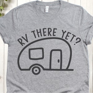 May include: A gray t-shirt with rolled-up sleeves featuring a black graphic of a camper and the text "RV THERE YET?". The design includes a camper outline with a door, window, and wheel, perfect for camping enthusiasts.