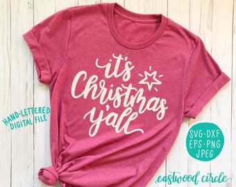 May include: Pink t-shirt with white text that reads "it's Christmas y'all".