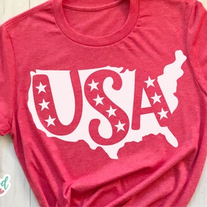 May include: Red t-shirt with a white outline of the United States of America and the word "USA" inside. The letters are decorated with white stars.