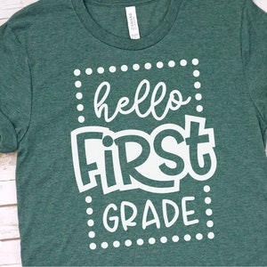 May include: A green t-shirt with the words "hello FIRST GRADE" in white, framed by a dotted border. The shirt has rolled-up sleeves and a crew neck. The brand "Eastwood Circle" is printed on the bottom left.