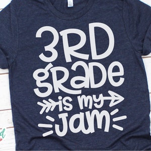 Op de afbeelding: Een marineblauw T-shirt met witte tekst die "3rd grade is my jam" zegt met pijlen aan beide kanten van "is my".