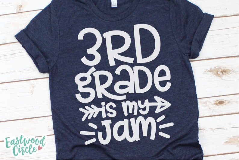 Op de afbeelding: Een marineblauw T-shirt met witte tekst die "3rd grade is my jam" zegt met pijlen aan beide kanten van "is my".